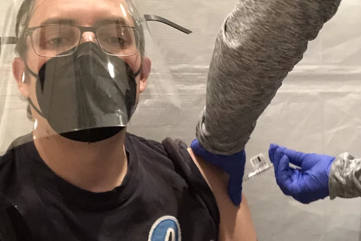 A lab member wearing a mask and face shield is seen getting vaccinated.